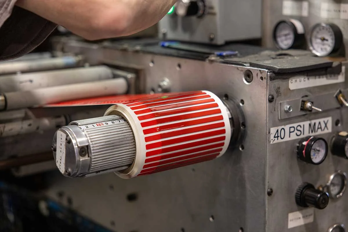 Close-up of a mechanical device with a cylindrical element decorated with red and white stripes, attached to a metal machine with gauges and a label indicating 40 PSI maximum pressure.