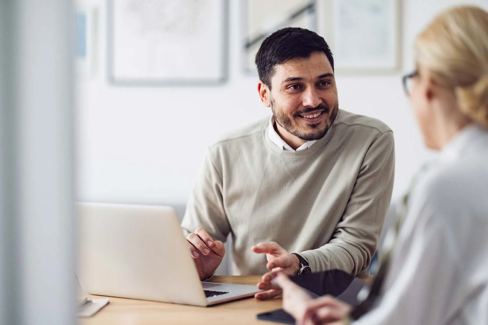 Man smiling and talking with a woman in an office setting, with a laptop on the table.